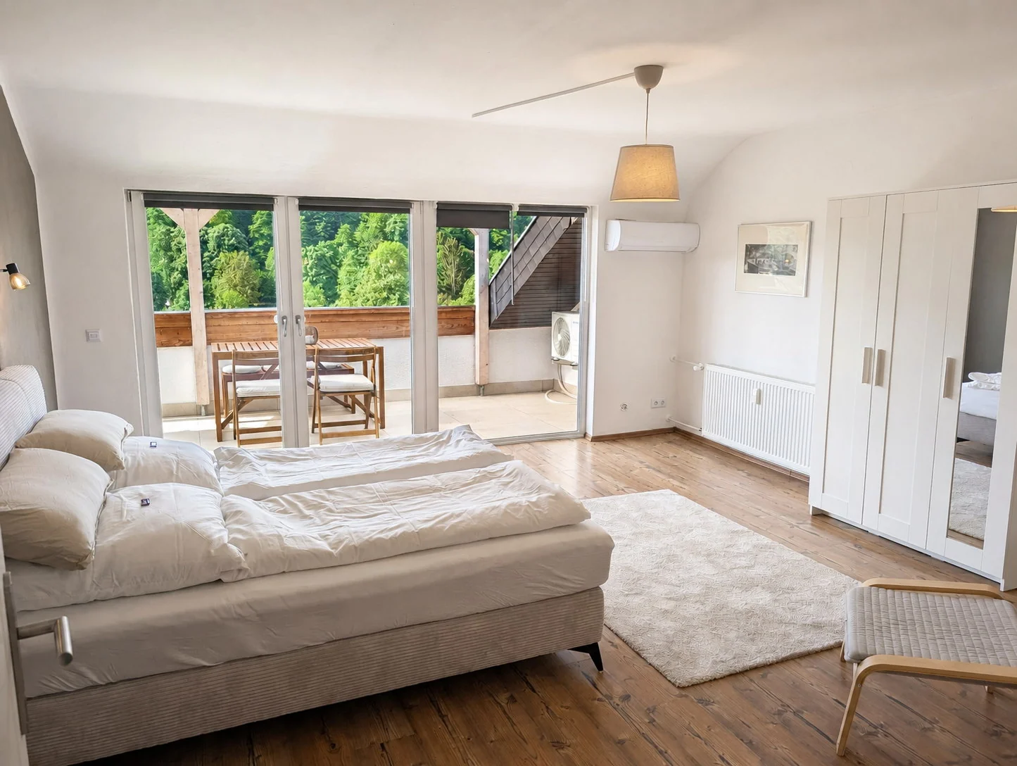 Großes Schlafzimmer mit bezogenem Doppelbett, Kleiderschrank und Balkonzugang